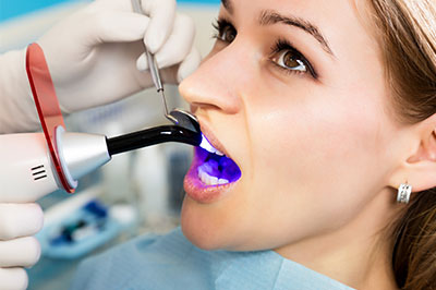 A woman receiving dental treatment, with a dental hygienist using an ultrasonic scaler on her teeth.