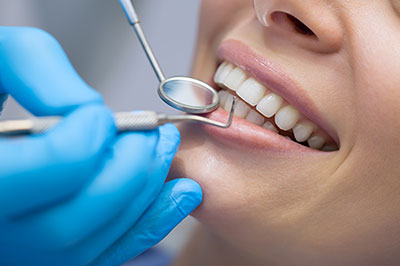 A woman receiving dental care with a smiling expression while wearing a blue protective glove.