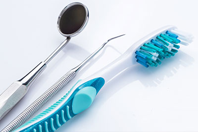 A collection of dental tools including a toothbrush with blue bristles, a metal dental mirror, and other instruments against a white background.