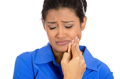 A woman with her mouth open, wearing a blue shirt, appears to be experiencing discomfort or pain, possibly related to dental care or oral health concerns.