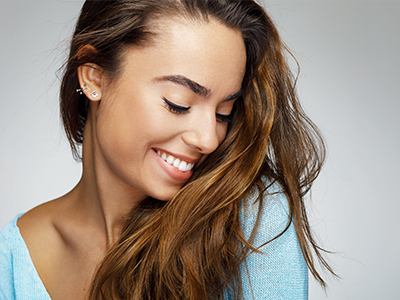 The image features a young woman with long hair smiling at the camera while looking down towards her shoulder.