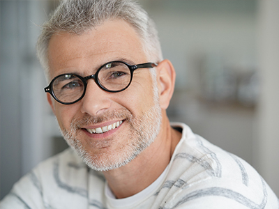 The image shows a man with glasses smiling at the camera, wearing a white shirt with a patterned collar.