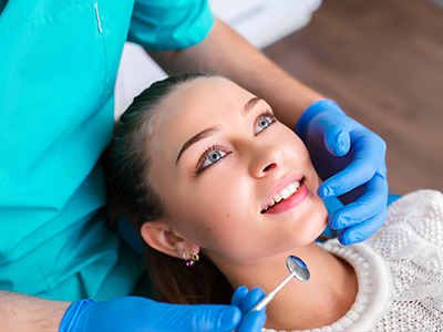 The image depicts a dental hygiene professional performing a procedure on a seated patient with a smiling expression.